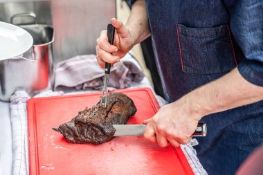 Şef bıçakla kesilmiş sigara içen biri kırmızı kesim tahtasının üzerinde et filetosu tüttürmüş ve BBC Southfood temalı ızgara yapıyor