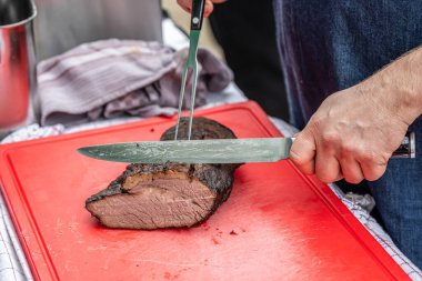 Şef bıçakla kesilmiş sigara içen biri kırmızı kesim tahtasının üzerinde et filetosu tüttürmüş ve BBC Southfood temalı ızgara yapıyor