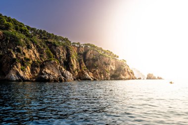 Costa Brava kıyılarının manzarası kayalık uçurumlar, yemyeşil yemyeşil ve ılık gün batımında parlayan sakin deniz suları..