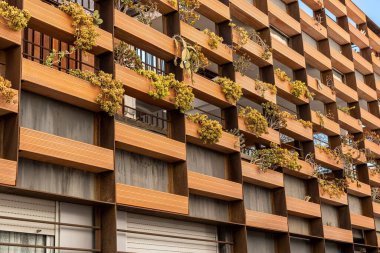 Şehirde dikey bahçeleri ve pencereleri gökyüzünü yansıtan bir apartman. Düşük açılı bir bakış açısıyla büyüleyici bir mimari beceri..