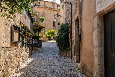 Tossa de mar 'da dar bir sokak, İspanya' nın eski kasabasında beyaz duvarlar, kaldırım taşları ve bol bitkiler var.
