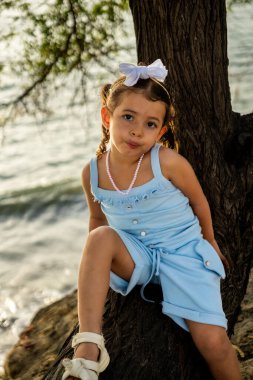 Latin bir kız Santa Marta Okyanusu 'nun arkasındaki ağaçta günbatımında Kolombiya' da mutlu bir şekilde oturuyor. Turizm, çocuk tatilleri, çeşitlilik ve Latin Amerika kavramları. Yüksek kalite fotoğraf