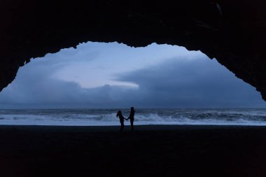 Genç ve sevgi dolu bir çift geç akşam İzlanda'da siyah plaj boyunca yürüyor