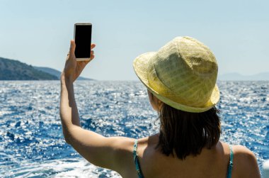 Geri kalan beyaz smartphone yat güneşli gün arka plan kopya alanı üstten görünüm hafta sonları deniz suyu üzerinde tutarak yaz şapkalı kadın tatil