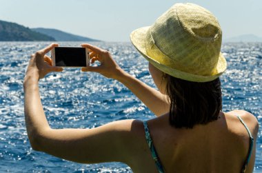 Geri kalan beyaz smartphone yat güneşli gün arka plan kopya alanı üstten görünüm hafta sonları deniz suyu üzerinde tutarak yaz şapkalı kadın tatil