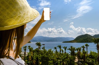 Gülümseyen kadın rahat sarı şapka smartphone deniz beach palm dağ güneşli bir gün bir arka plan üzerinde tutarak yaz tatili portresi