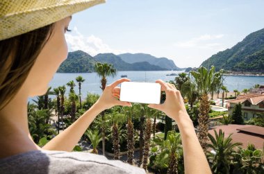 Gülümseyen kadın rahat sarı şapka smartphone deniz beach palm dağ güneşli bir gün bir arka plan üzerinde tutarak yaz tatili portresi