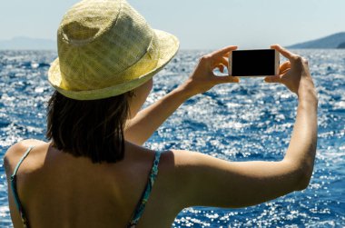 Geri kalan beyaz smartphone yat güneşli gün arka plan kopya alanı üstten görünüm hafta sonları deniz suyu üzerinde tutarak yaz şapkalı kadın tatil