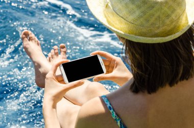 Geri kalan beyaz smartphone yat güneşli gün arka plan kopya alanı üstten görünüm hafta sonları deniz suyu üzerinde tutarak yaz şapkalı kadın tatil