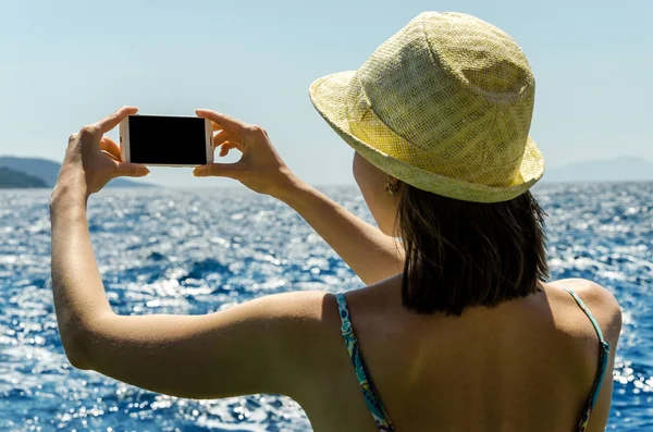 Geri kalan beyaz smartphone yat güneşli gün arka plan kopya alanı üstten görünüm hafta sonları deniz suyu üzerinde tutarak yaz şapkalı kadın tatil