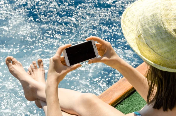 Geri kalan beyaz smartphone yat güneşli gün arka plan kopya alanı üstten görünüm hafta sonları deniz suyu üzerinde tutarak yaz şapkalı kadın tatil