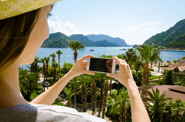 Gülümseyen kadın rahat sarı şapka smartphone deniz beach palm dağ güneşli bir gün bir arka plan üzerinde tutarak yaz tatili portresi