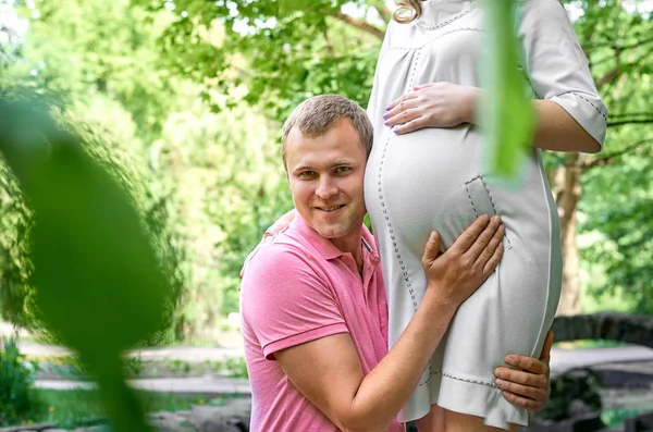 Handsome man is listening to his beautiful pregnant wife\'s tummy belly and smiling. Husband listening to his wife\'s belly. Happy pregnant family funny.