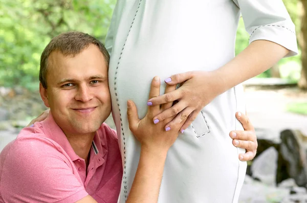 Handsome man is listening to his beautiful pregnant wife\'s tummy belly and smiling. Husband listening to his wife\'s belly. Happy pregnant family funny.