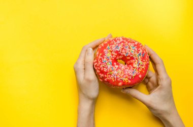 Kadın el ile pembe çörek tutarak ekstra kalori yağ lokanta aşırı kilo sağlıksız sarı zemin üzerine sprinkles.