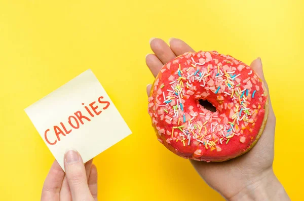 女性手捧粉红色甜甜圈与洒额外的卡路里脂肪快餐过量体重不健康的黄色背景 — 图库照片