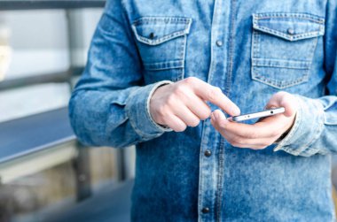 Yakın kadar Hipster iş adamı kullanarak akıllı cep telefonu App açık siyah Oled ekran arka plan Denim Jeans Gömlek şık giyinmiş