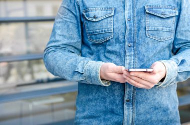 Yakın kadar Hipster iş adamı kullanarak akıllı cep telefonu App açık siyah Oled ekran arka plan Denim Jeans Gömlek şık giyinmiş