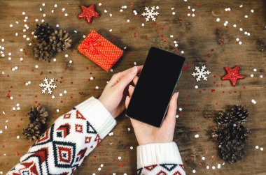 Noel hediye kar taneleri ve kar ile ahşap arka plan üzerinde akıllı cep telefonu ile oled göstermek tutarak sıcak örme kazak kadın elinde. Mutlu yeni yıl ve Xmas düz kompozisyon üstten görünüm yatıyordu.