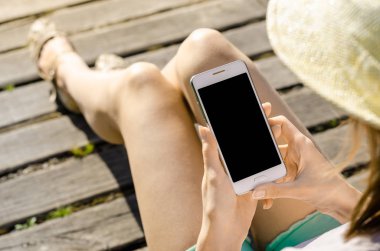 Yakın kadar iş kadını şapka kullanma Smartphone cep telefonu açık siyah Oled ekran ahşap arka plan şık yaz giyinmiş hipster içinde