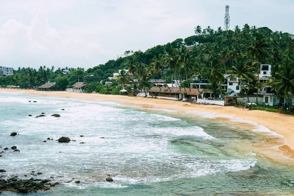 Αμμουδιά με γαλαζοπράσινα καθαρά νερά της θάλασσας, και μερικοί άνθρωποι στην παραλία. Mirisa Σρι Λάνκα — Φωτογραφία Αρχείου