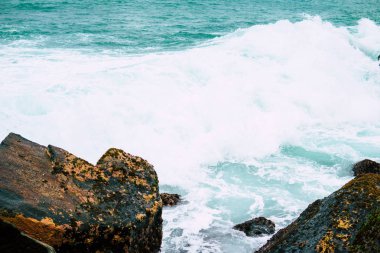 sahil kumu üzerinde dağınık kayalar kapatın. Sığ derinlik-in tarla. Seçici odak ön plan buzlu. Çok renkli taşların farklı şekil ve boyutlarda, okyanus dalgaları, bulutlu gökyüzü arka plan bulanık