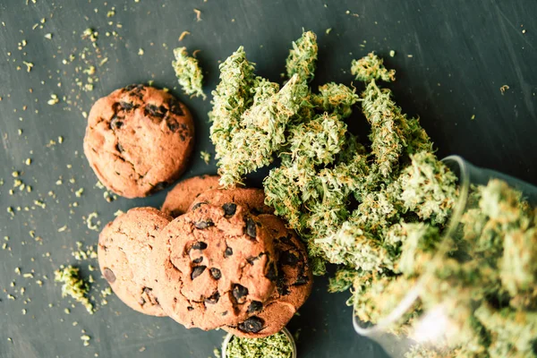 Galletas con cannabis y cogollos de marihuana sobre la mesa. Concepto de cocina con hierba de cannabis. Tratamiento de la marihuana medicinal para su uso en alimentos, sobre un fondo negro — Foto de Stock