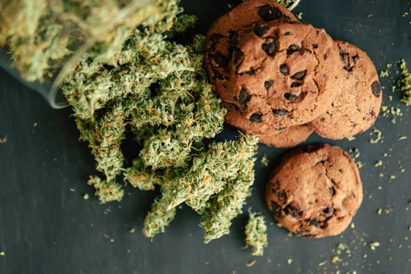 Cozinhar com erva de cannabis. Tratamento de maconha medicinal para uso em alimentos, Em um fundo preto Cookies com cannabis e botões de maconha na mesa. Conceito de — Fotografia de Stock