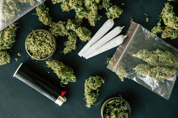 Cannabis gezamenlijke en een pakje van onkruid en Smartphone op een zwarte houten achtergrond. Bud marijuana bloemen op schalen, slijper en versnipperde — Stockfoto