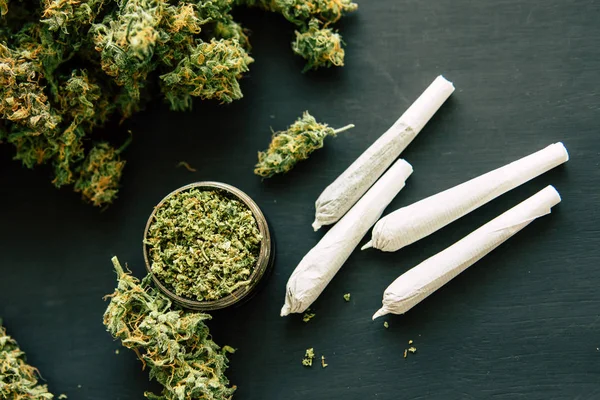 Unkraut auf dem Hintergrund einer schwarzen Tischplatte mit zerkleinerten Cannabisblüten und Joint und — Stockfoto