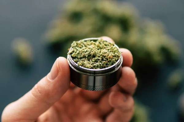 De flores de cannabis y escamas y junta vista superior en la mano un molinillo para moler marihuana hierba sobre un fondo — Foto de Stock