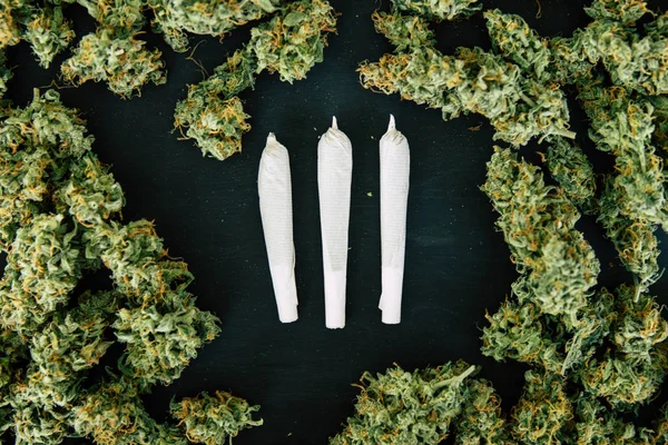 Flores y la articulación y la maleza en el fondo de una mesa de madera negro vista superior amoladora con cannabis triturado —  Fotos de Stock
