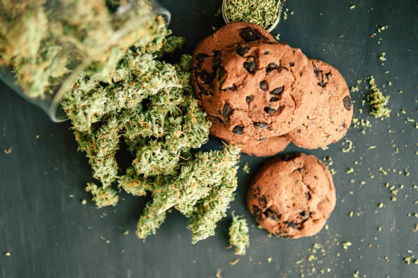 Lékařské marihuany pro použití v potravinách Cbd, na černém pozadí sušenky s konopím a pupeny marihuany na stůl. — Stock fotografie