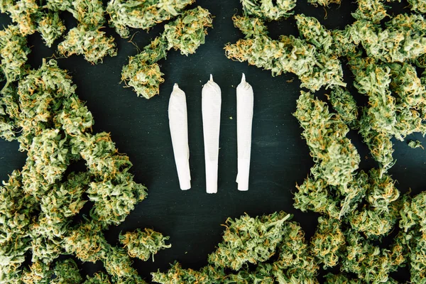 Amoladora con flores de cannabis trituradas y Articulación y maleza en el fondo de una mesa de madera negra vista superior —  Fotos de Stock