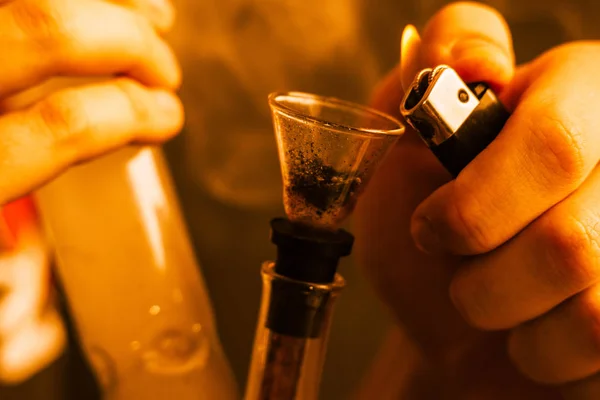 Um homem fuma erva de cannabis, Bong mais leve nas mãos. Fumaça na tonificação amarela — Fotografia de Stock