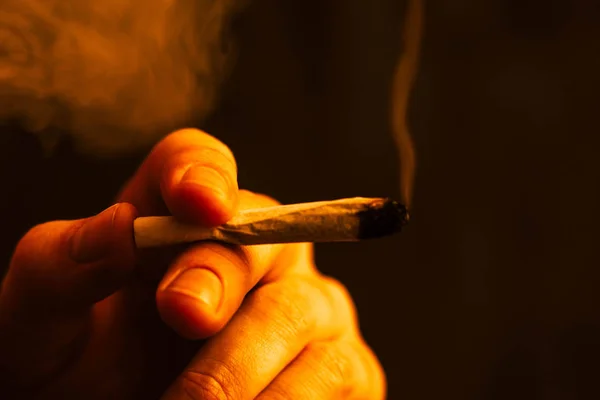 Joint in man hand. A man smokes cannabis weed, a . Smoke on a Yellow toning — Stock Photo, Image