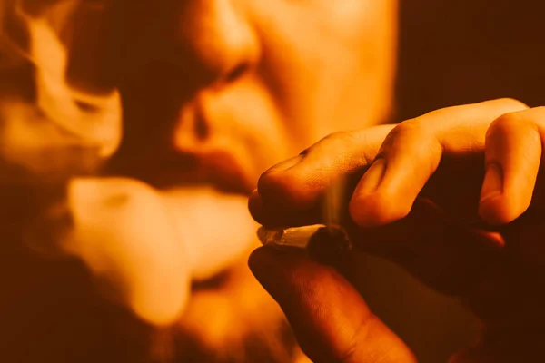 En man röker weed cannabis en gemensam och en tändare i handen. Gul toning — Stockfoto