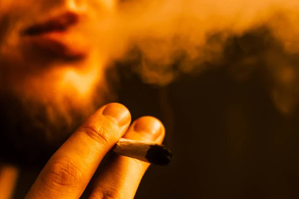 Ένας άνθρωπος καπνίζει κάνναβη ζιζανίων, ένα κοινό και ένα ελαφρύτερο στα χέρια του. Κίτρινο τόνωση — Φωτογραφία Αρχείου