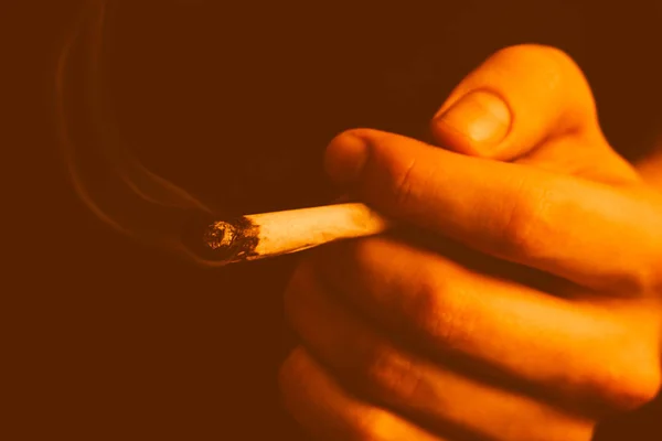 Joint in man hand. A man smokes cannabis weed, a . Smoke on a Yellow toning — Stock Photo, Image