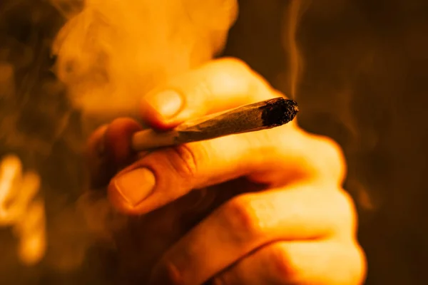 Gemensamma i hand. En man röker cannabis ogräs, en. Rök på en svart, gul toning — Stockfoto