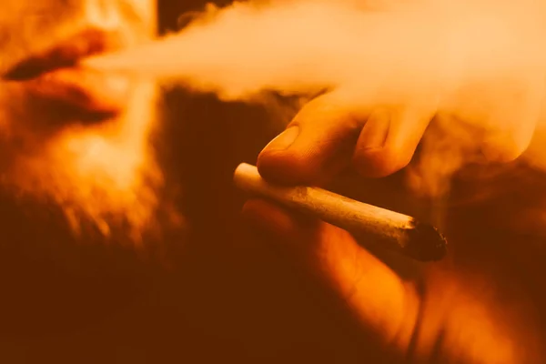 A joint in hand A man smokes cannabis weed, . Smoke on a black Yellow toning — Stock Photo, Image