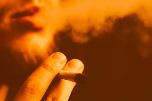 Un uomo fuma erba di cannabis, una canna e un accendino in mano. Tonificante giallo — Foto Stock