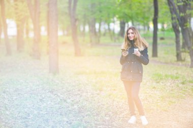 Bir kız sabah bir smartphone ve kahve ışık tonlama ile bir parkta yürüyüş