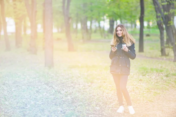 Bir kız sabah bir smartphone ve kahve ışık tonlama ile bir parkta yürüyüş