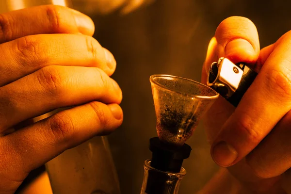 Um homem fuma erva de cannabis, um charro e um isqueiro nas mãos. Tonificação amarela — Fotografia de Stock