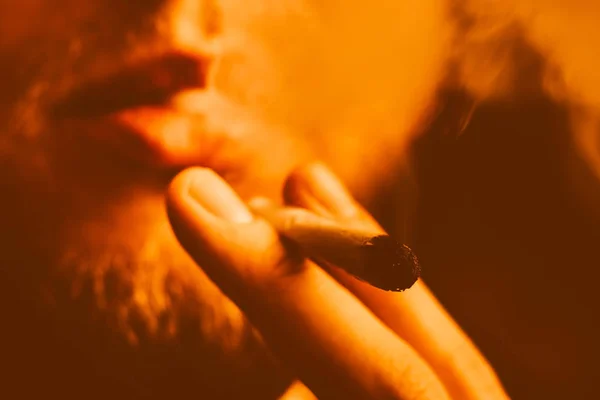 Humo sobre fondo negro. Un hombre fuma marihuana, una articulación tonificación amarilla — Foto de Stock
