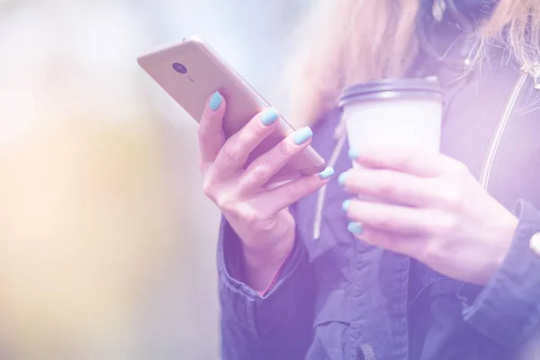 Una chica está caminando por la mañana en un parque con un teléfono inteligente y café, tonificación ligera — Foto de Stock
