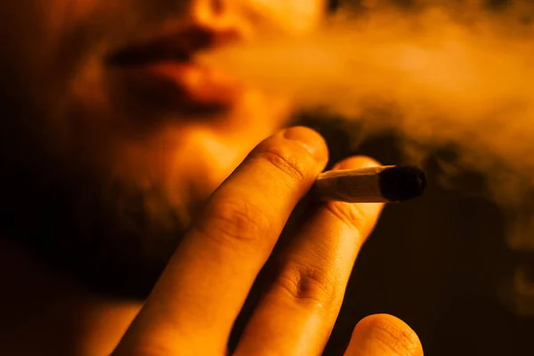 Muž kouří trávu konopí, společnou a zapalovač ve svých rukou. Žlutá tónování — Stock fotografie