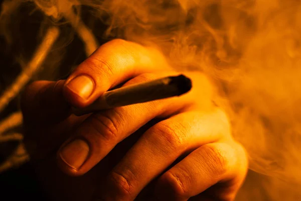 Cannabis ogräs, ett gemensamt i hans händer A man röker. Rök på en gul toning — Stockfoto