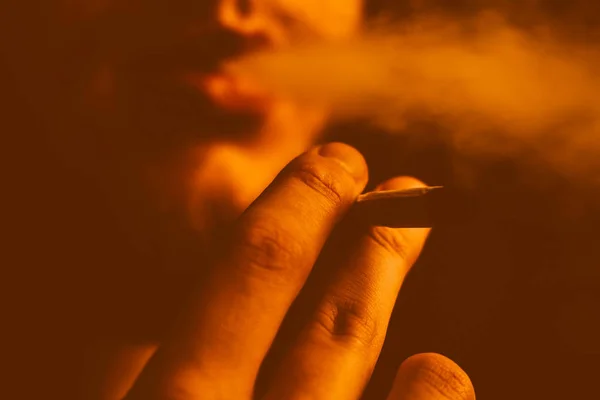 大麻杂草, 在他手中的一个男人抽烟的联合。黄色色调的烟雾 — 图库照片